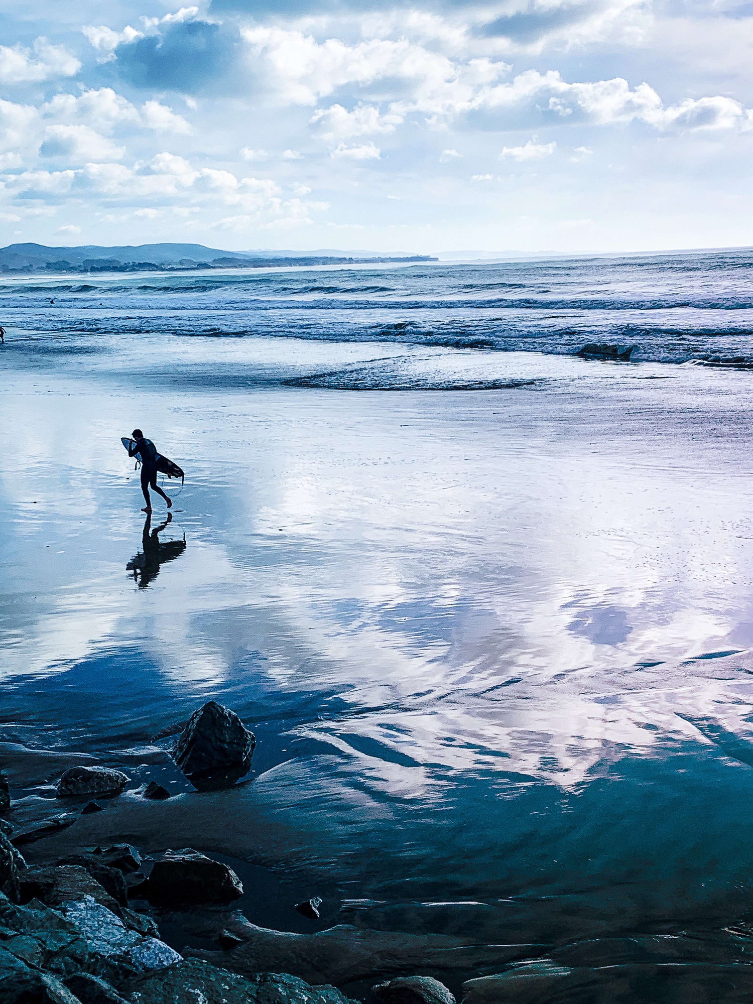 A surfer crossing wet sand at low tide